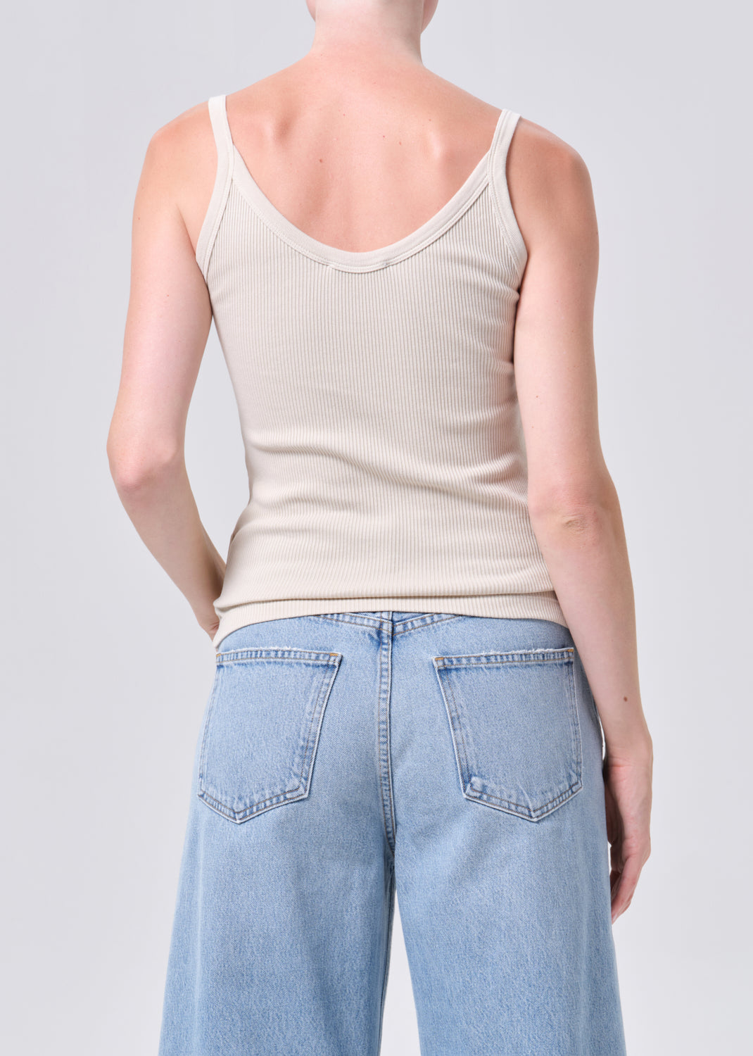 Person wearing a beige tank top and light blue jeans on a plain background