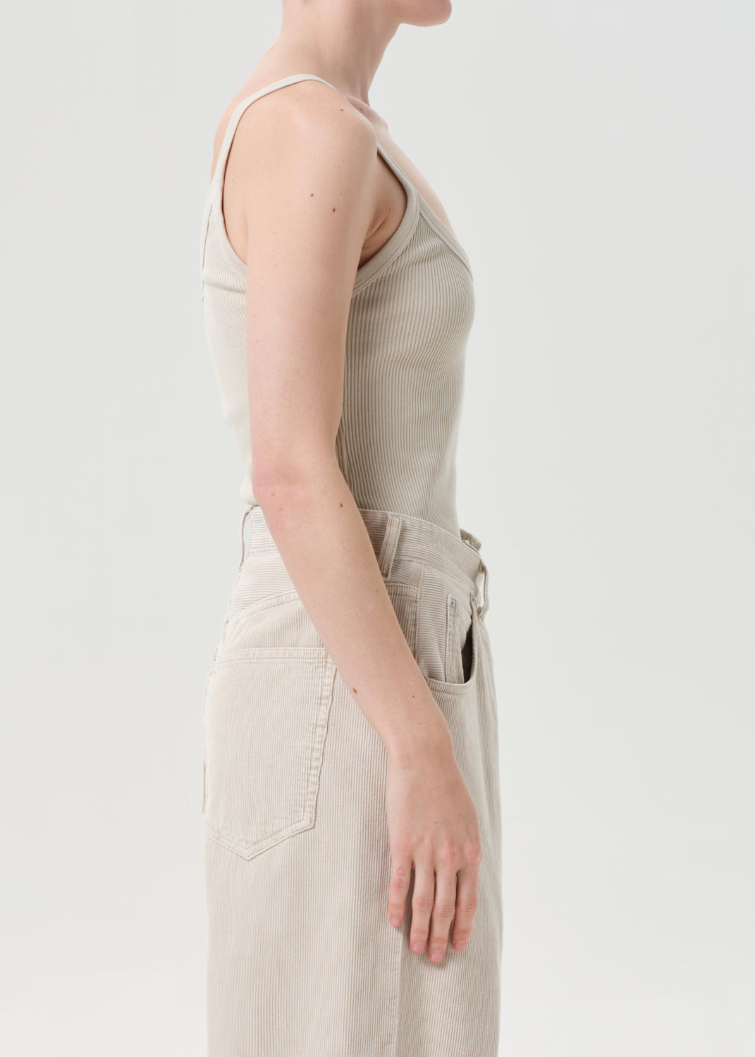 Person wearing a beige sleeveless top and pants on a white background