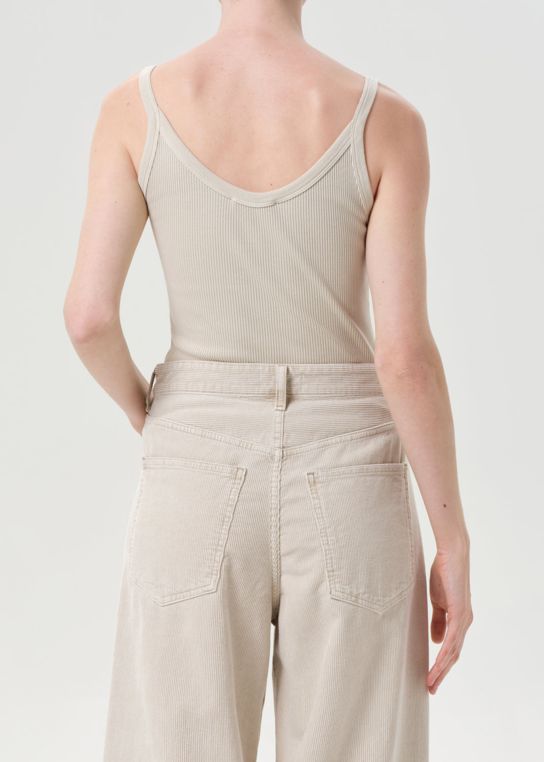 Person wearing a beige ribbed tank top and wide-leg pants on a light gray background
