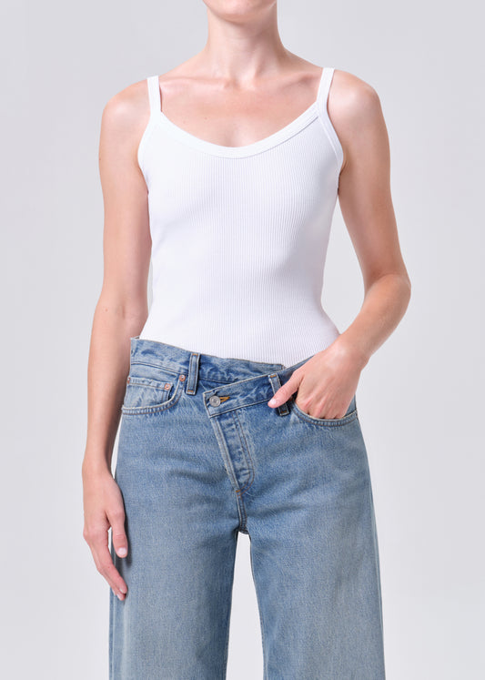 Person wearing a white tank top and light blue jeans on a plain background