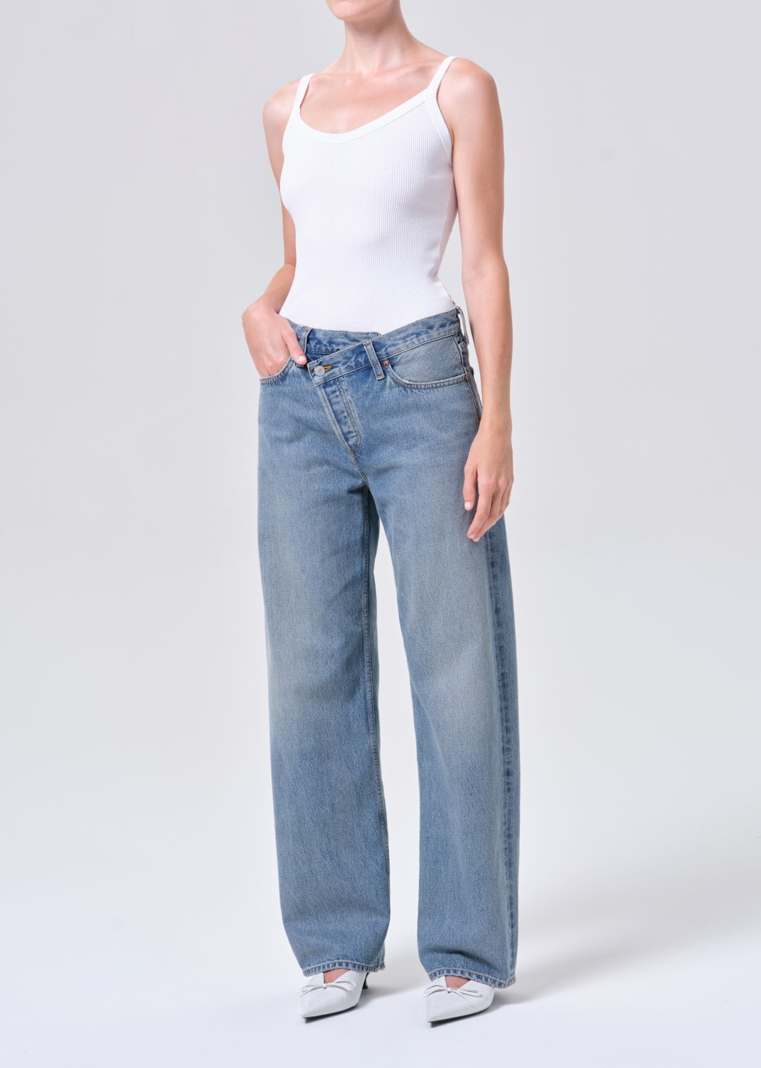 Person wearing light blue jeans and a white tank top on a white background