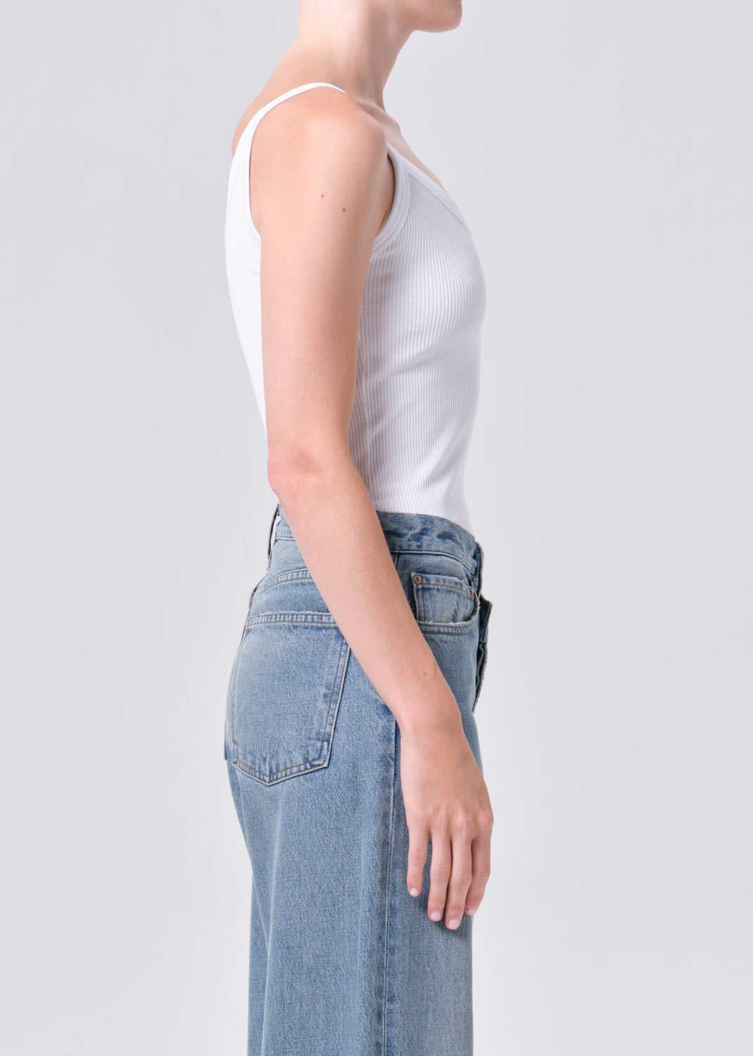 Person wearing a white tank top and light blue jeans on a plain background
