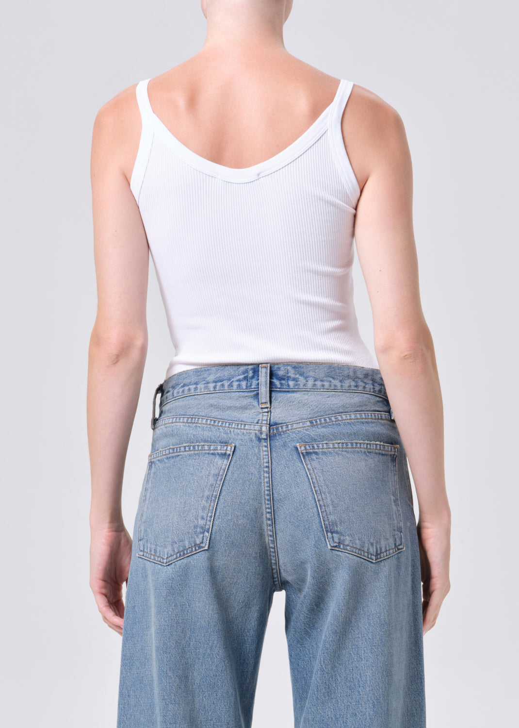 Person wearing a white tank top and blue jeans on a plain background