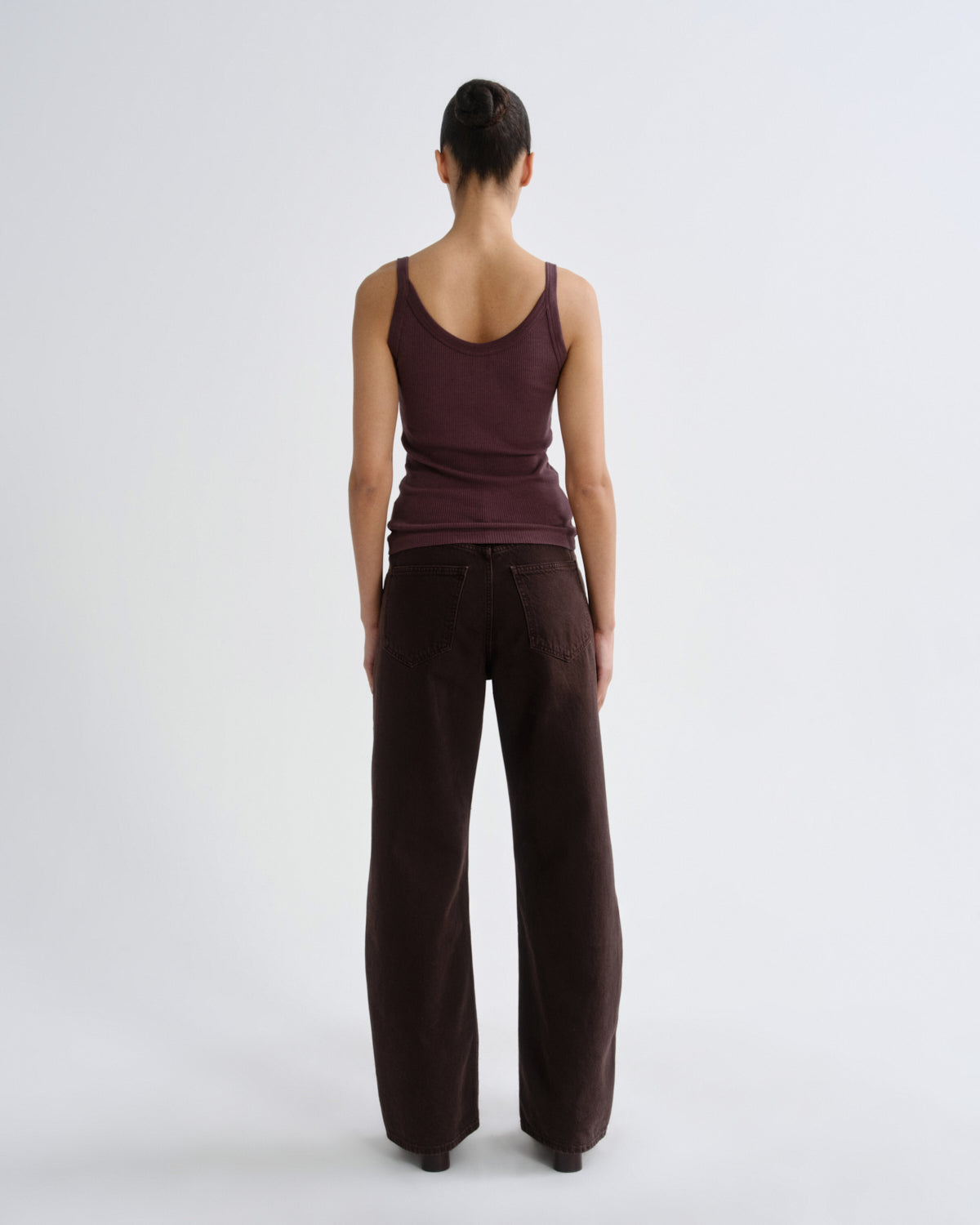 A model viewed from the back wearing a dark plum-brown ribbed tank top and matching wide-leg trousers against a light gray studio background.