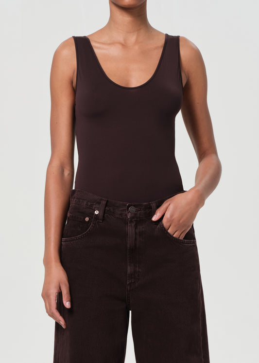 Person wearing a brown tank top and dark jeans on a light gray background