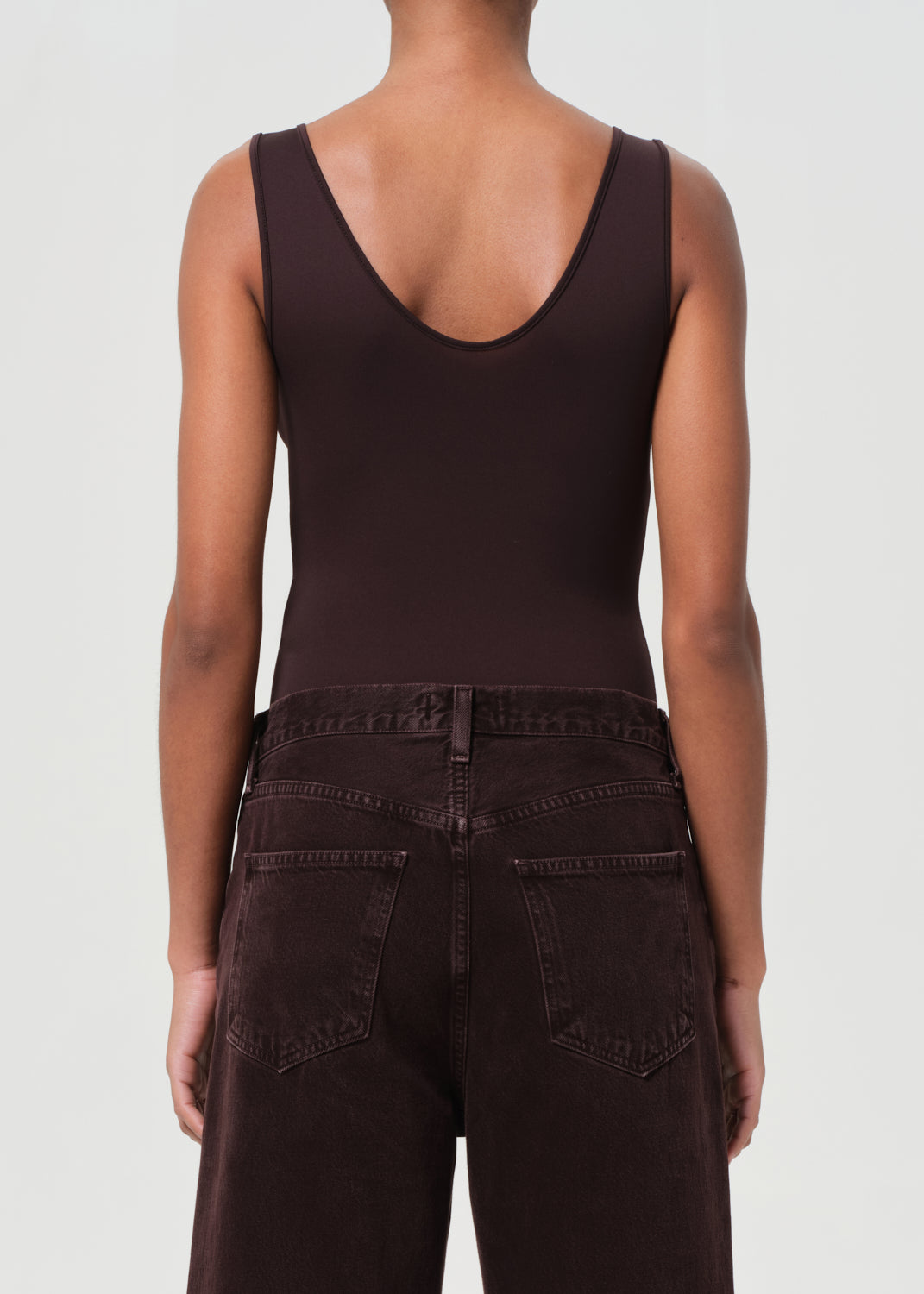 Person wearing a brown tank top and dark pants on a white background