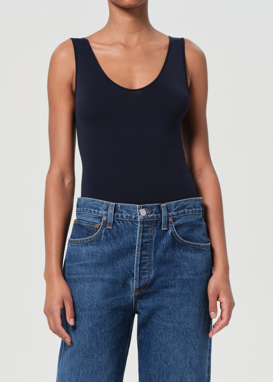Person wearing a navy bodysuit and blue jeans on a white background