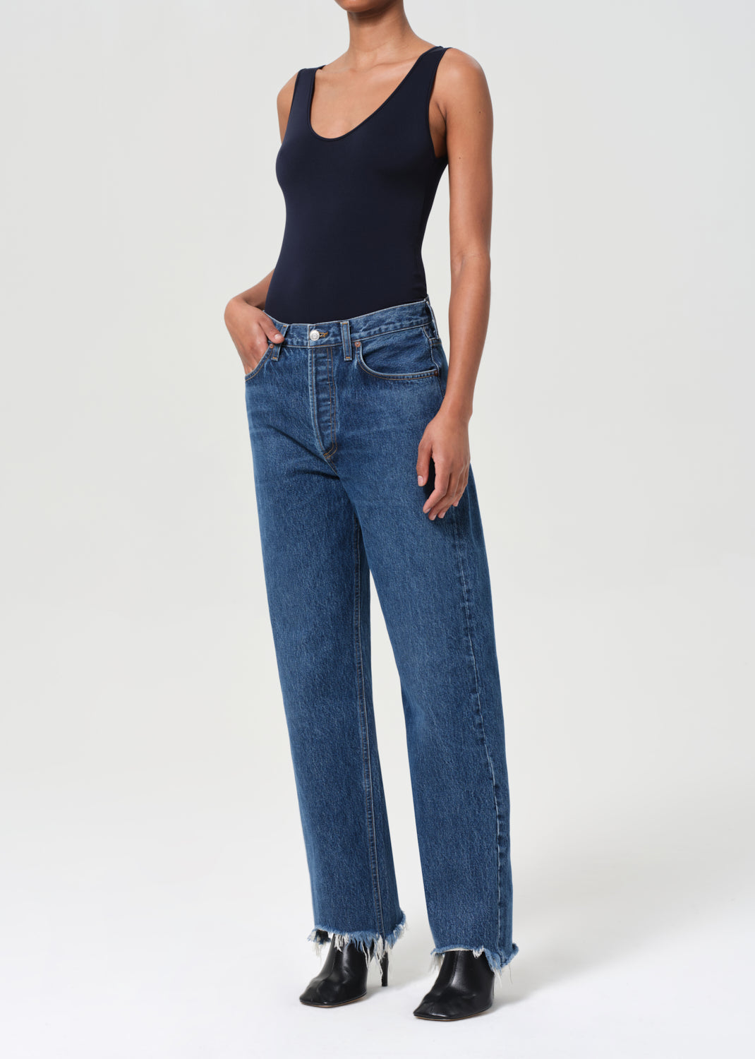 Person wearing a navy bodysuit and blue jeans on a white background