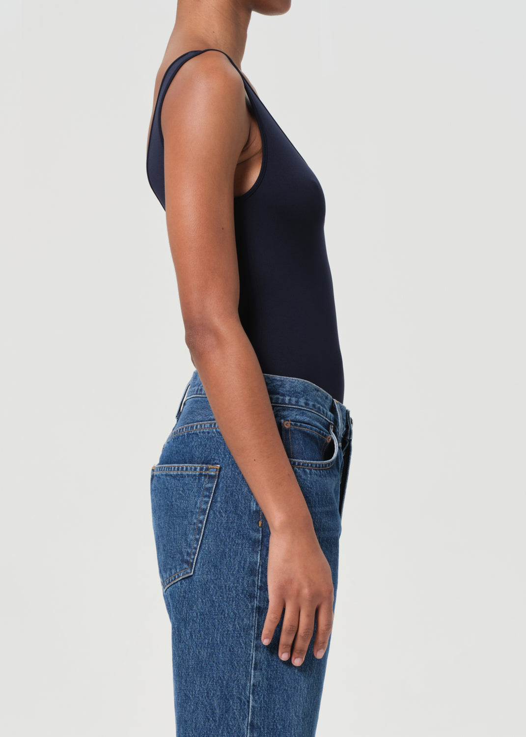 Person wearing a navy bodysuit and blue jeans on a light gray background