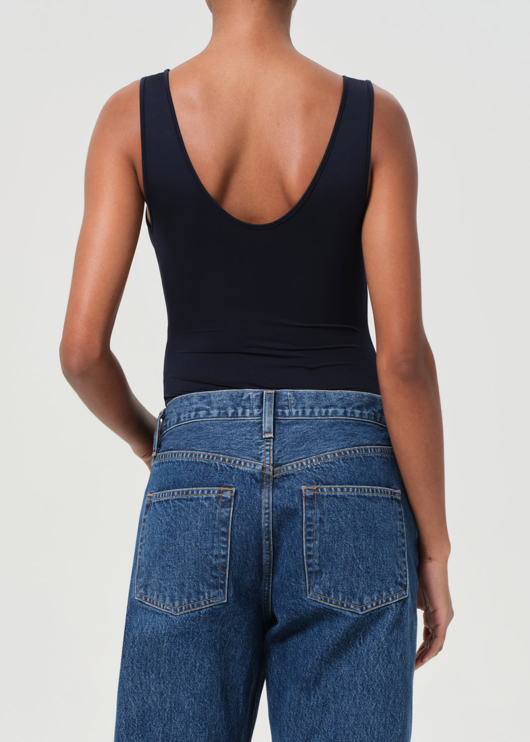 Person wearing a navy bodysuit and blue jeans on a plain background