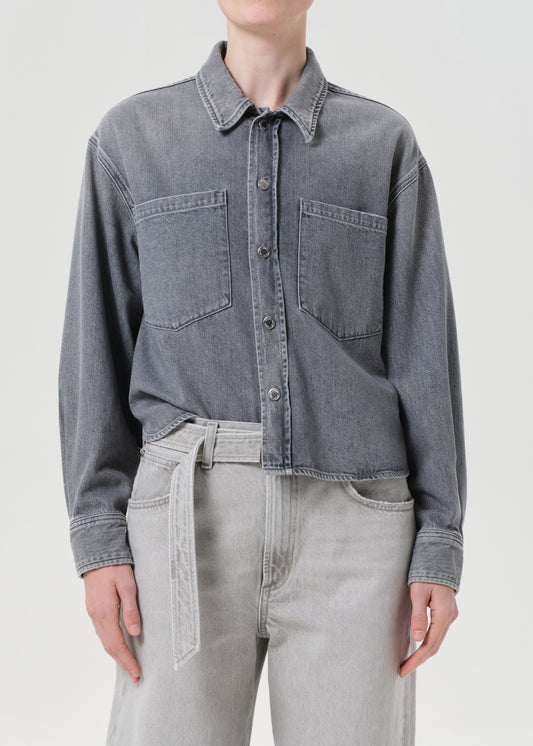 Person wearing a gray denim shirt and light gray pants on a white background