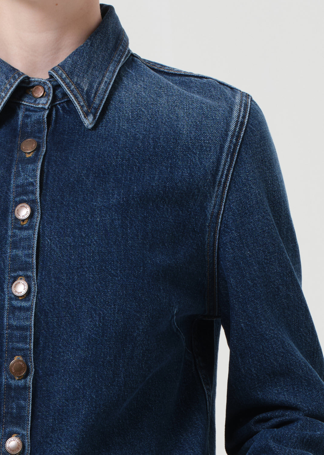 Close-up of a blue denim shirt with button details on a plain background