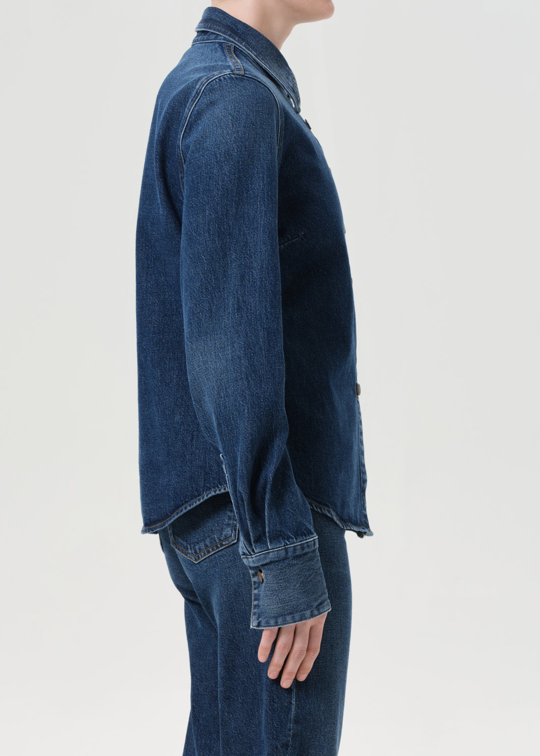 Person wearing a blue denim jacket and jeans on a light gray background