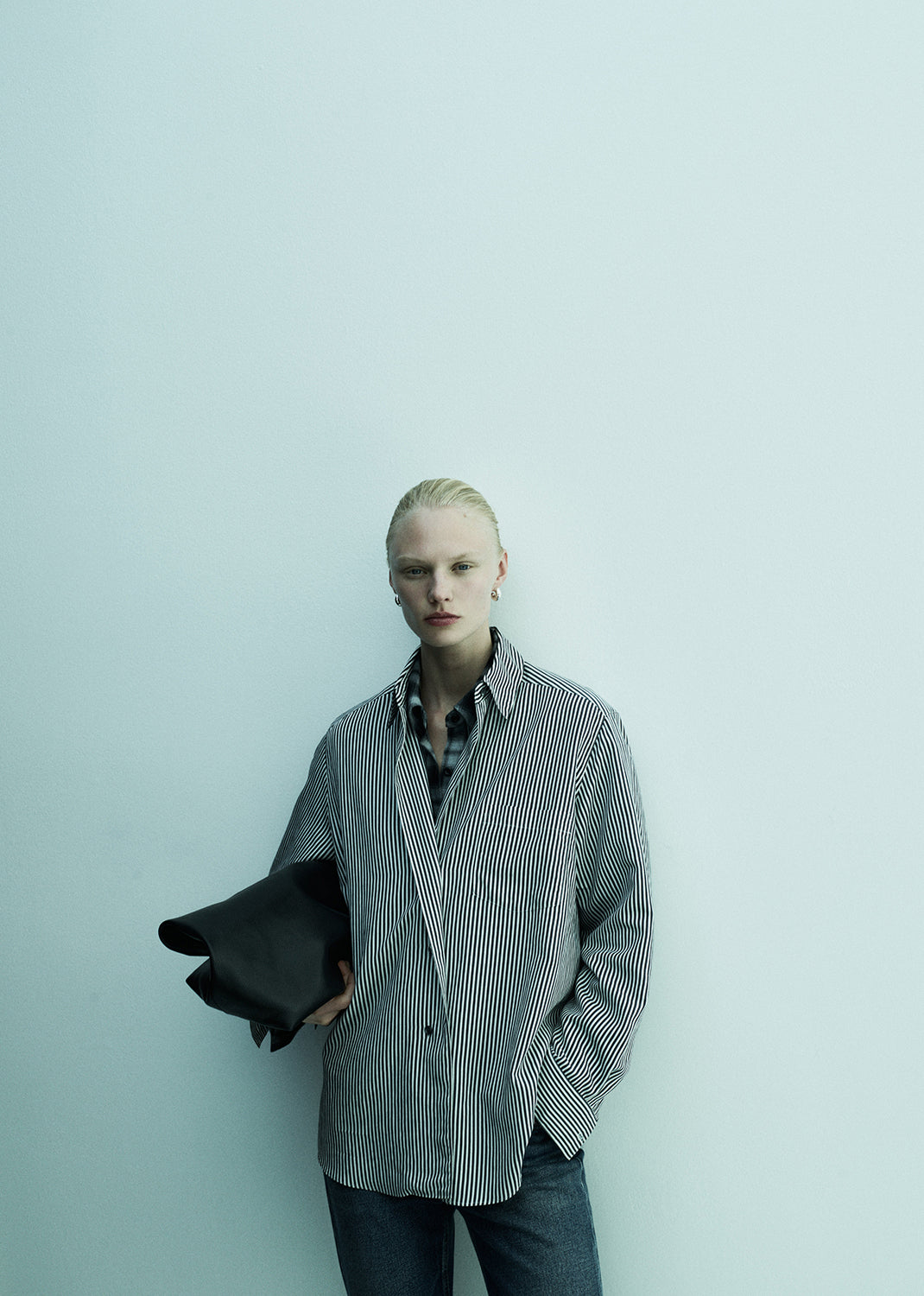 Person wearing a checkered shirt holding a jacket against a light background