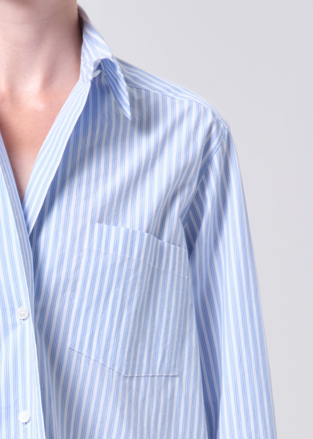 Close-up of a person wearing a light blue and white striped shirt against a gray background
