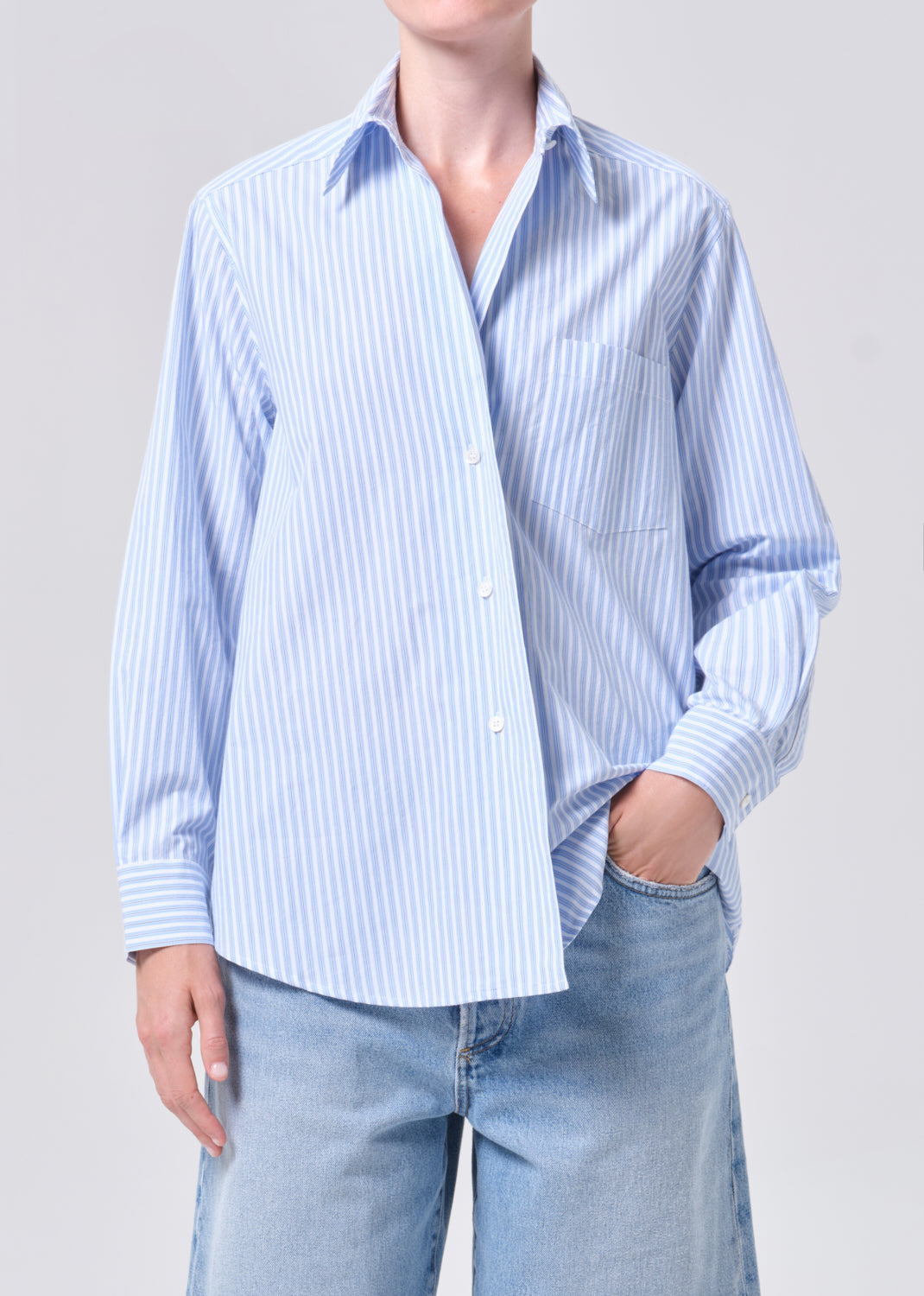 Person wearing a light blue and white striped shirt with rolled-up sleeves against a plain background