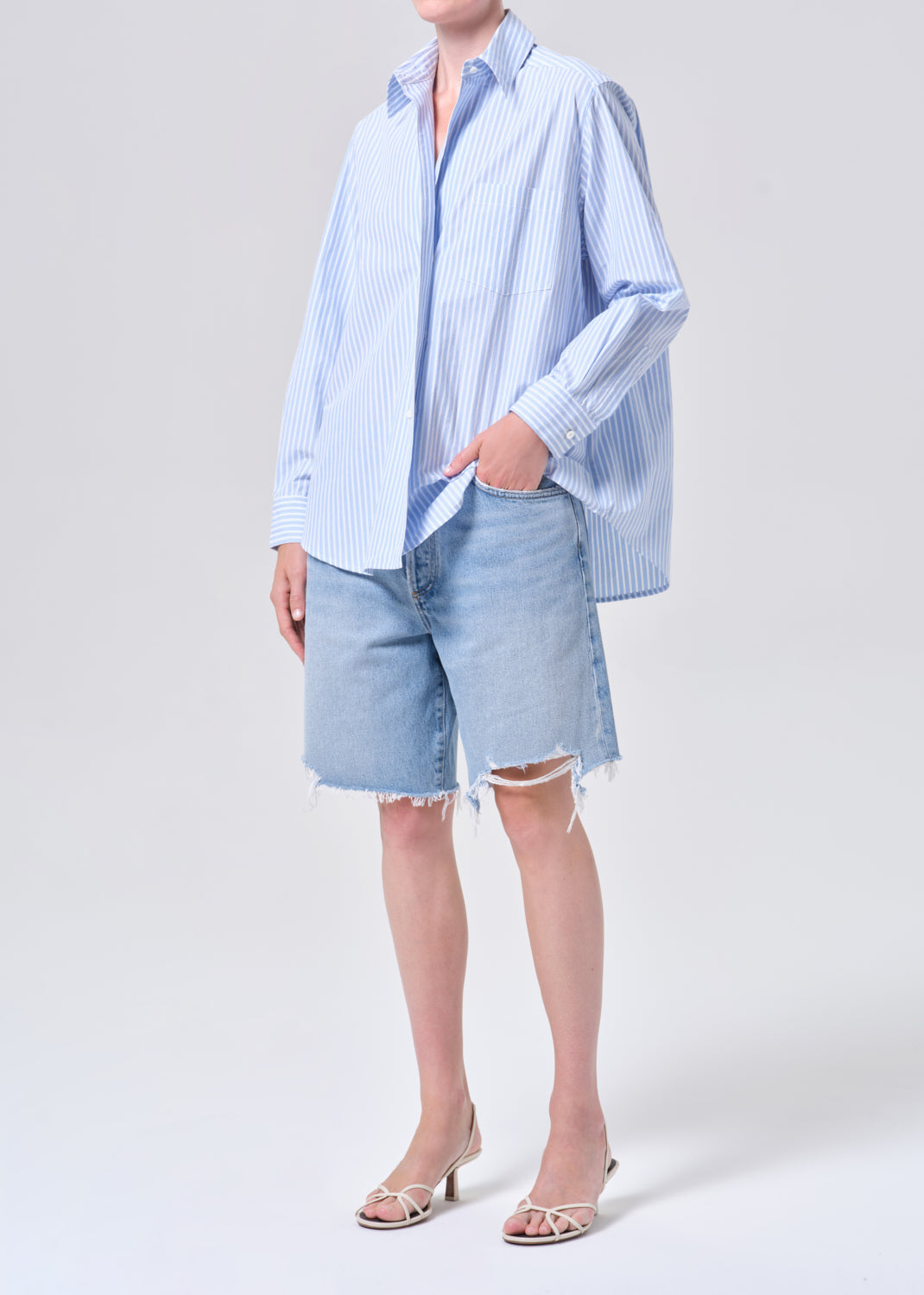 Person wearing a light blue striped shirt and denim shorts on a white background