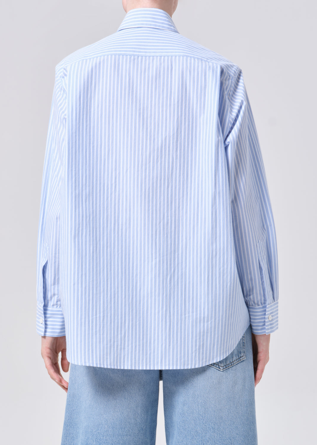 Person wearing a light blue striped shirt and jeans on a plain background