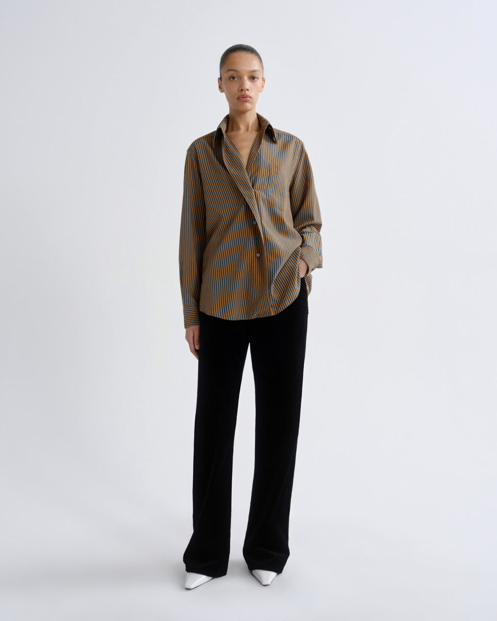 Person wearing a brown striped shirt and black pants on a white background