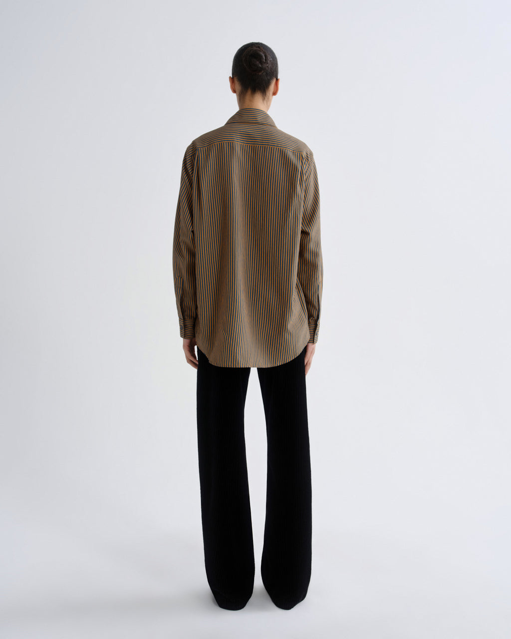 Person wearing a brown striped shirt and black pants on a white background