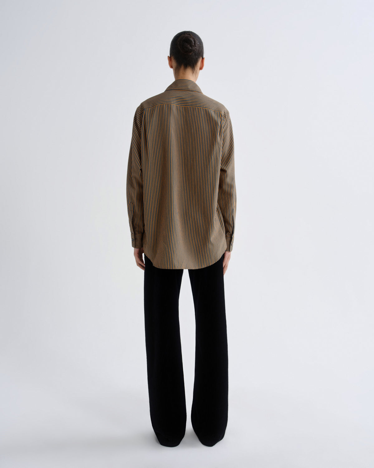 Person wearing a brown striped shirt and black pants on a white background