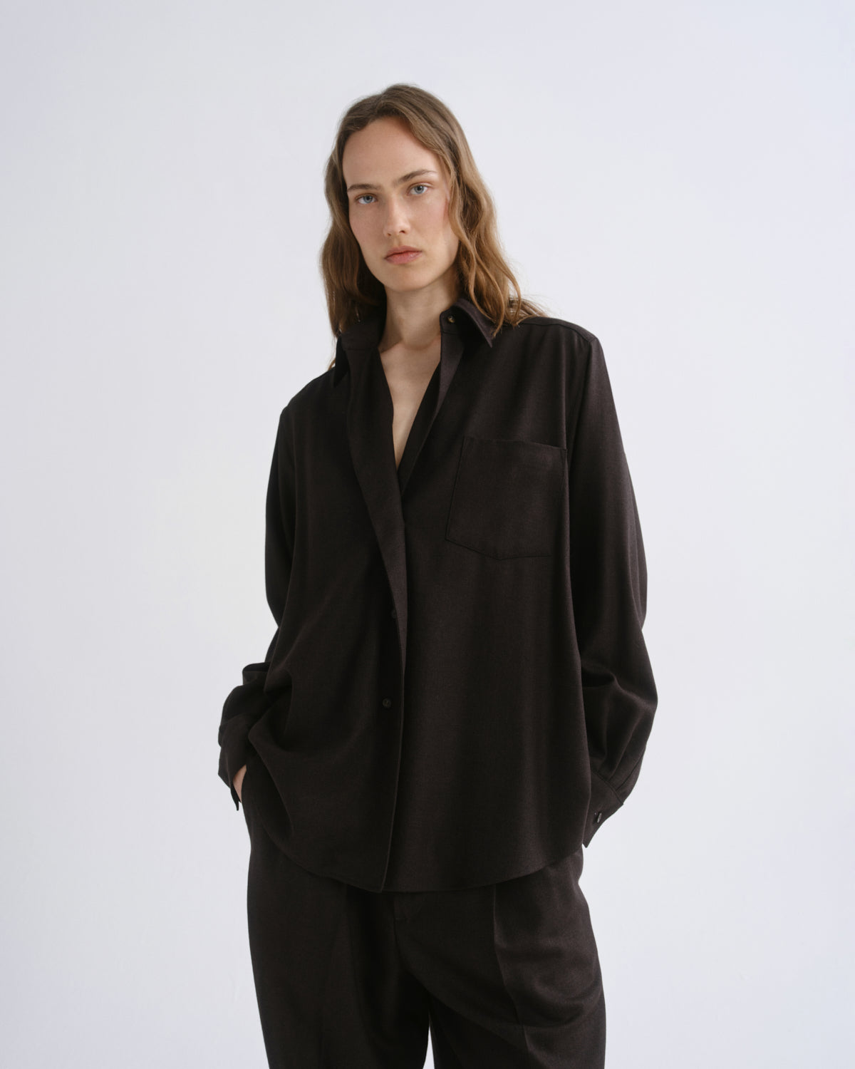 A woman modeling a loose-fitting black button-up shirt and matching black trousers against a grey background.