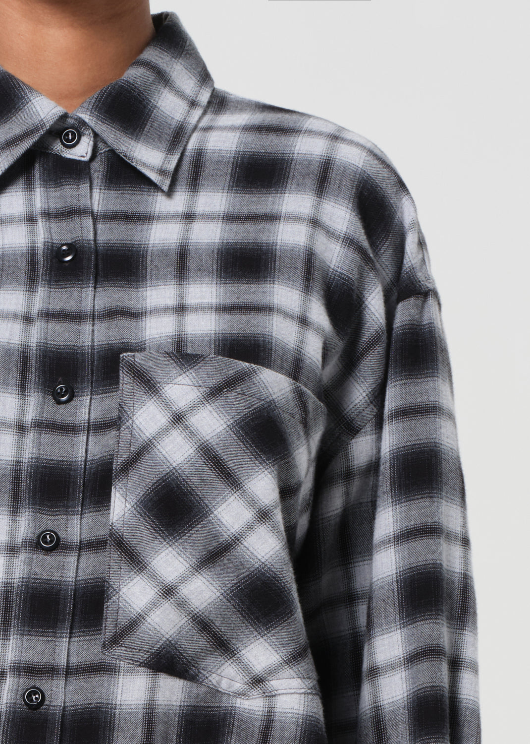 Close-up of a person wearing a black and gray plaid shirt with a pocket on a white background