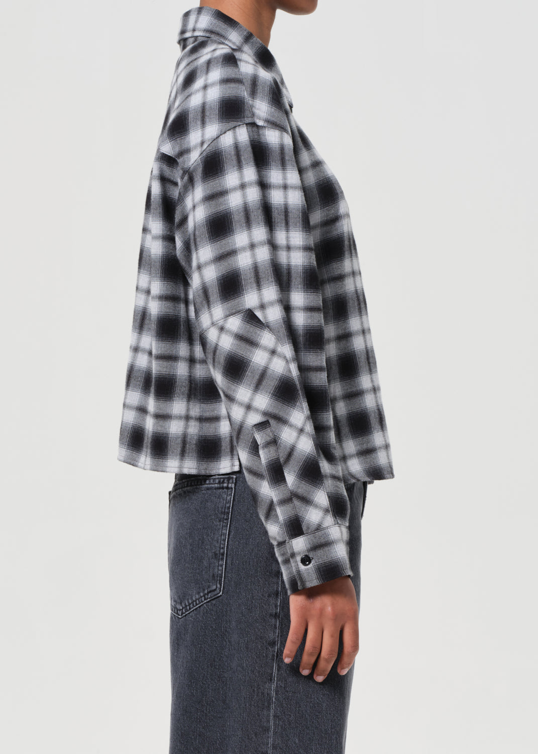 Person wearing a black and white plaid shirt with rolled-up sleeves on a plain background