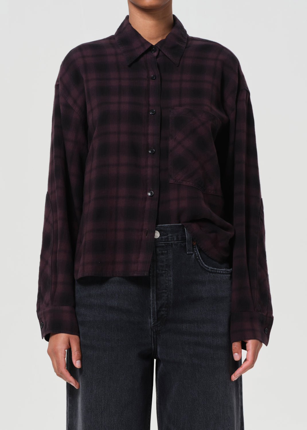 Person wearing a dark plaid shirt and black jeans on a white background