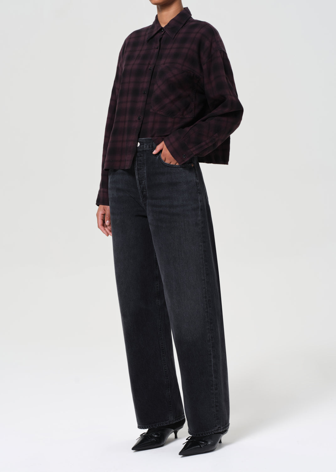 Person wearing a plaid shirt and black pants on a white background
