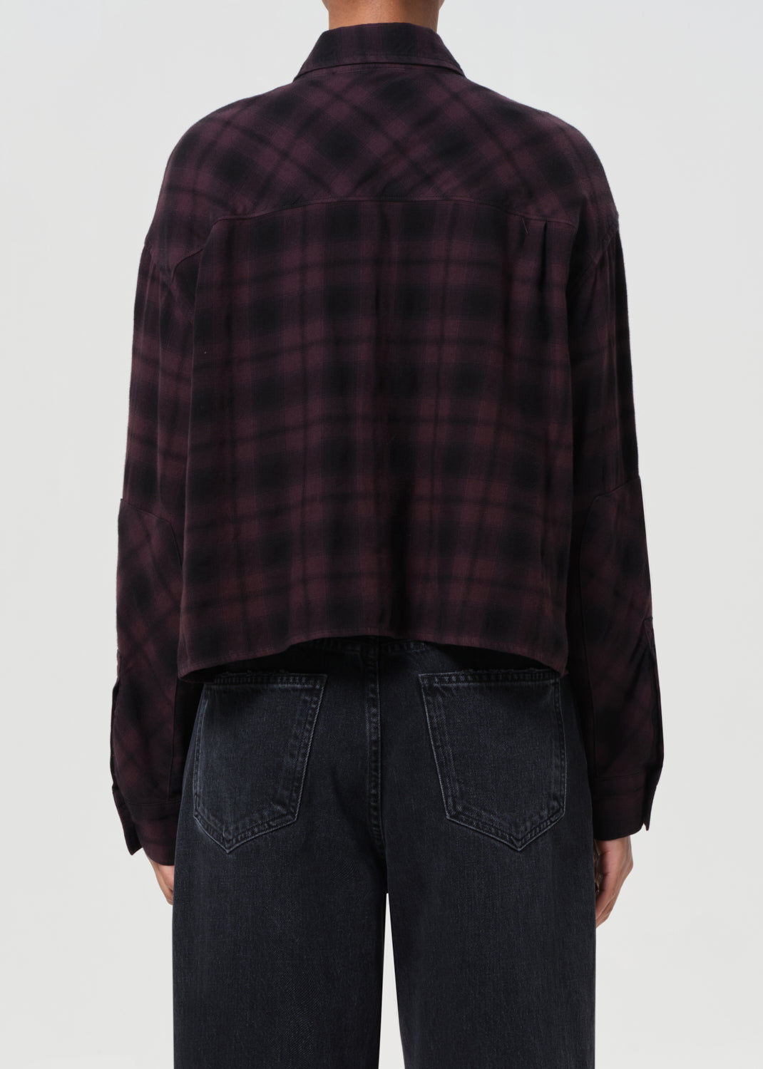 Person wearing a dark plaid shirt and black pants on a white background