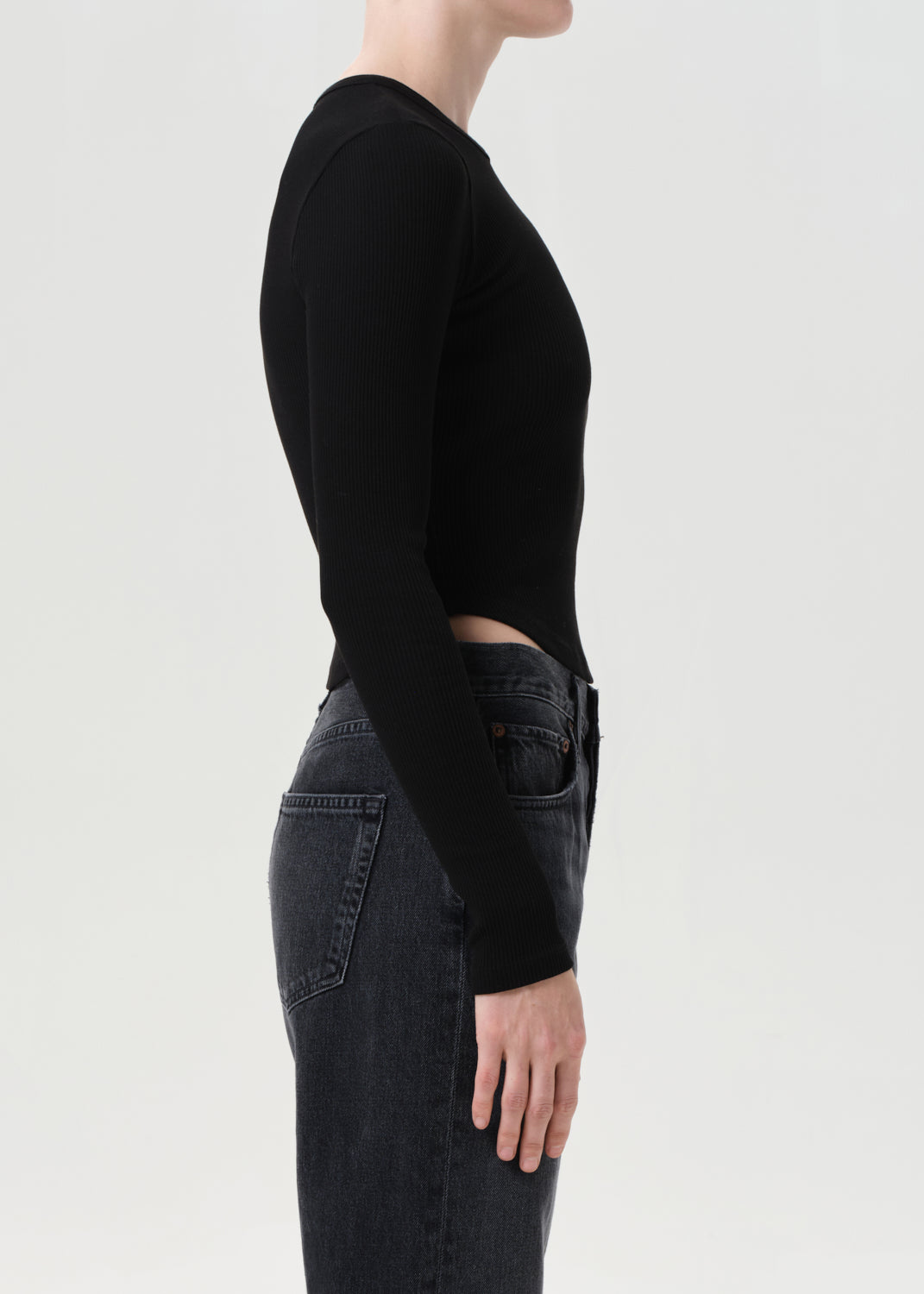 Person wearing a black long-sleeve top and dark jeans on a light gray background