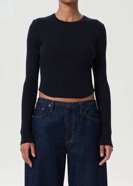 Person wearing a black long-sleeve crop top and dark blue jeans on a white background