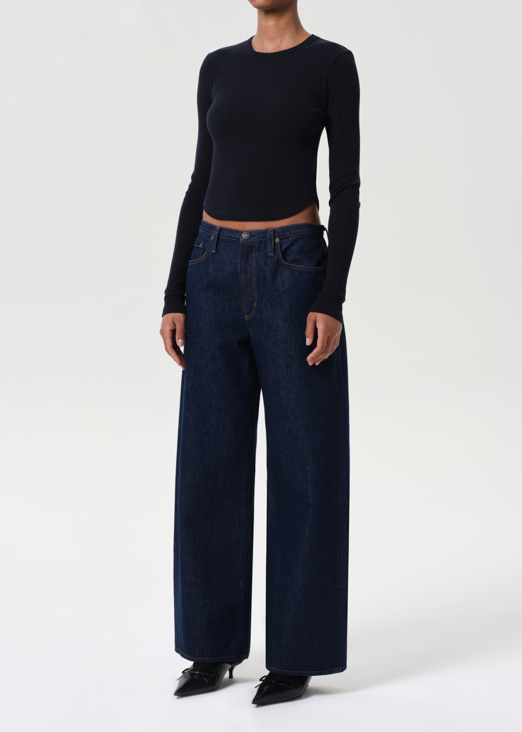 Person wearing a black long-sleeve top and dark blue jeans on a white background