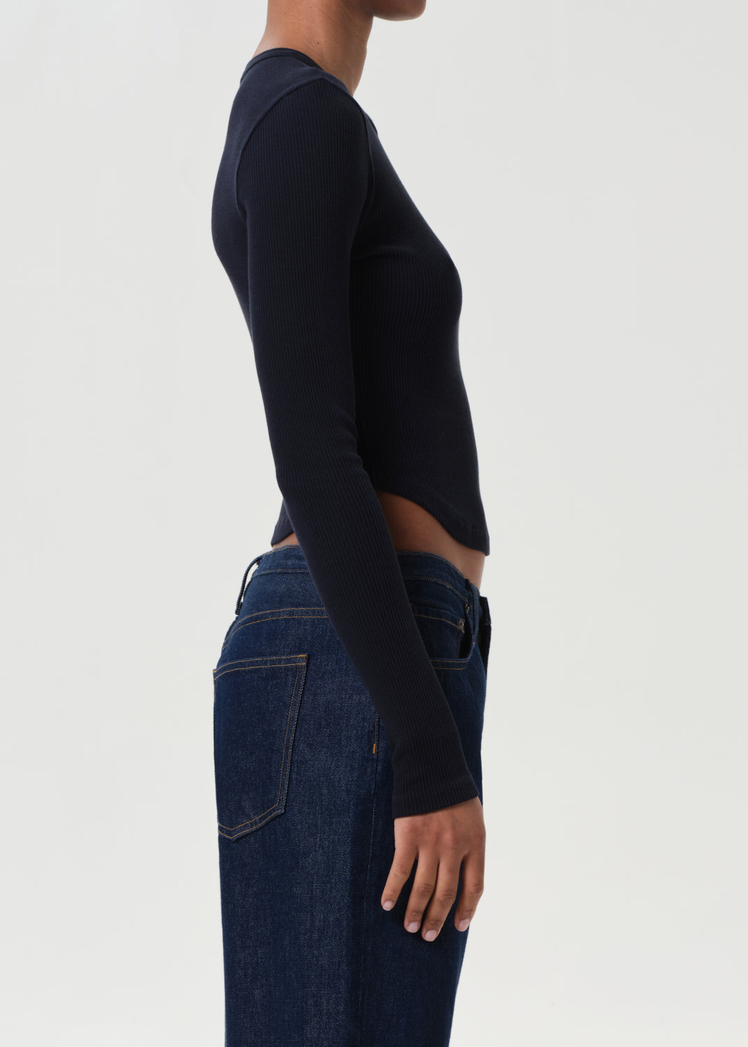 Person wearing a black long-sleeve top and blue jeans on a white background