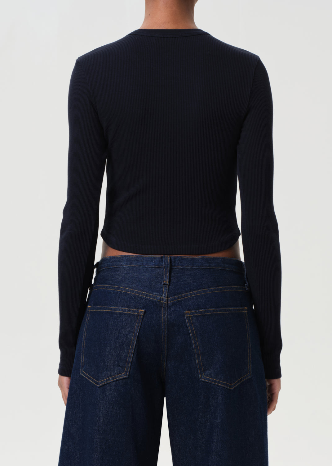 Person wearing a black long-sleeve top and blue jeans from behind on a white background