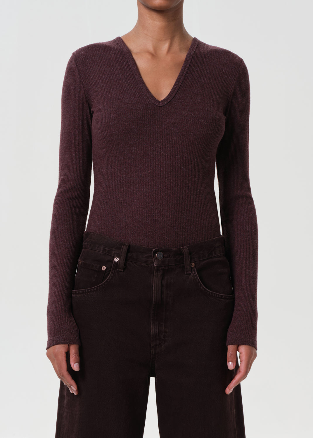 Person wearing a maroon long-sleeve top and dark jeans on a white background