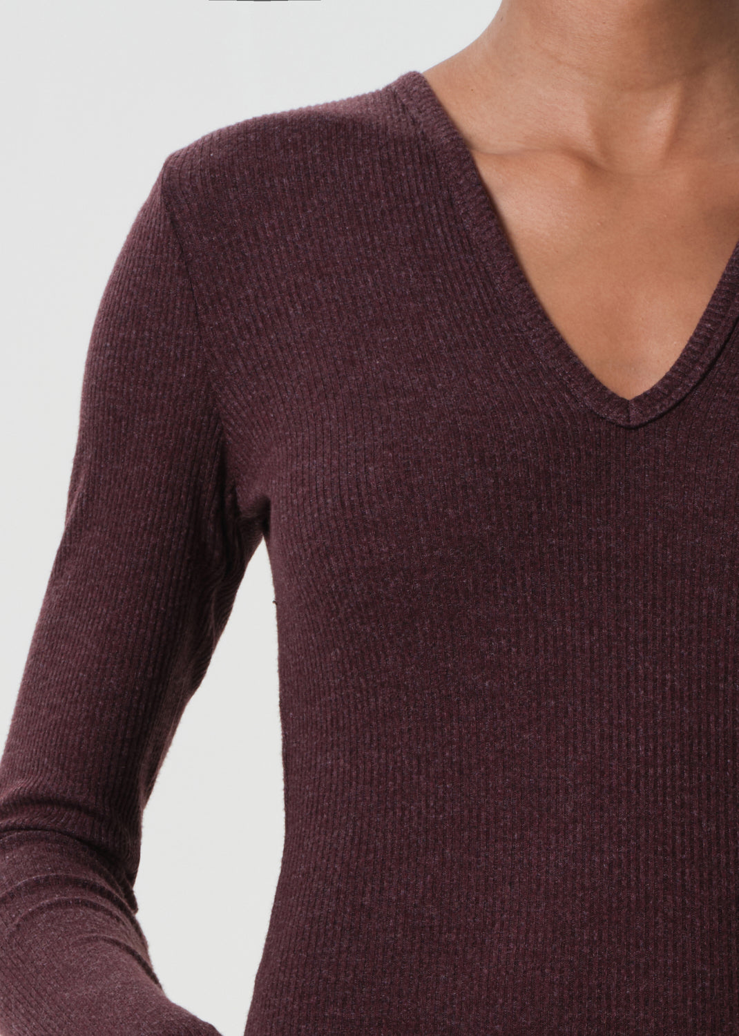 Close-up of a person wearing a dark purple ribbed sweater on a light gray background