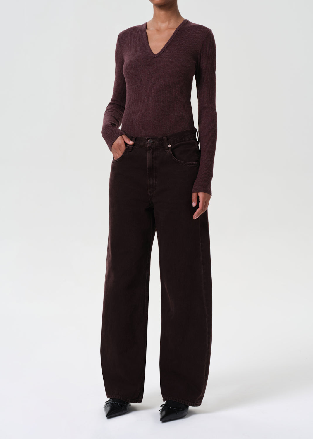 Person wearing a burgundy sweater and dark brown pants on a white background