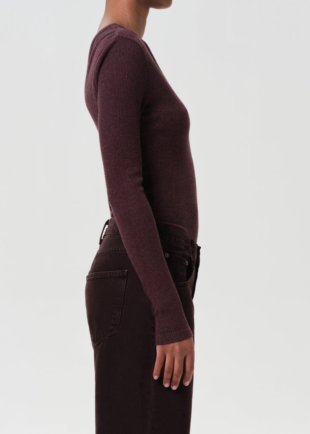 Person wearing a maroon long-sleeve top and dark pants on a light gray background