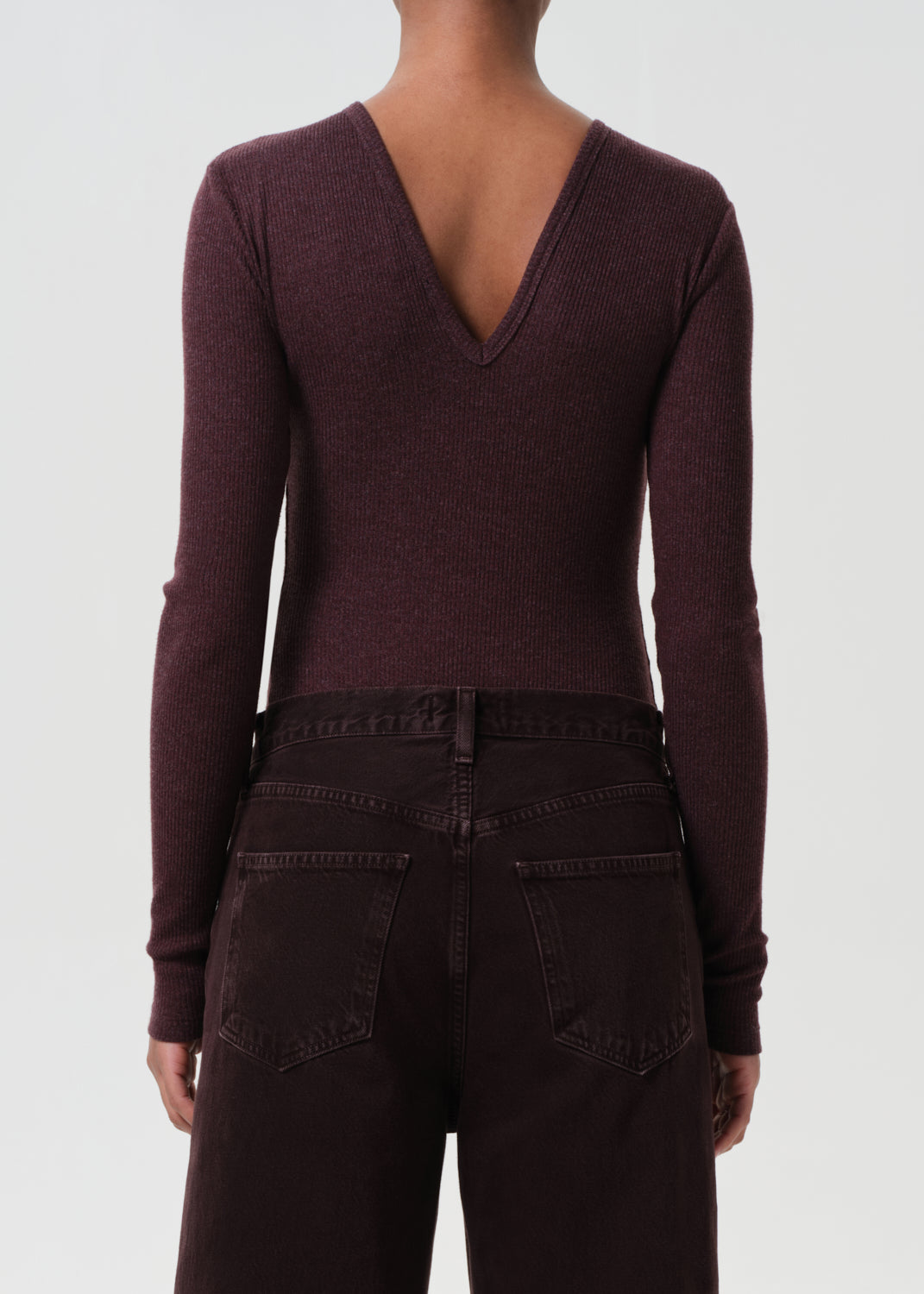 Person wearing a deep V-neck burgundy sweater and dark jeans on a white background
