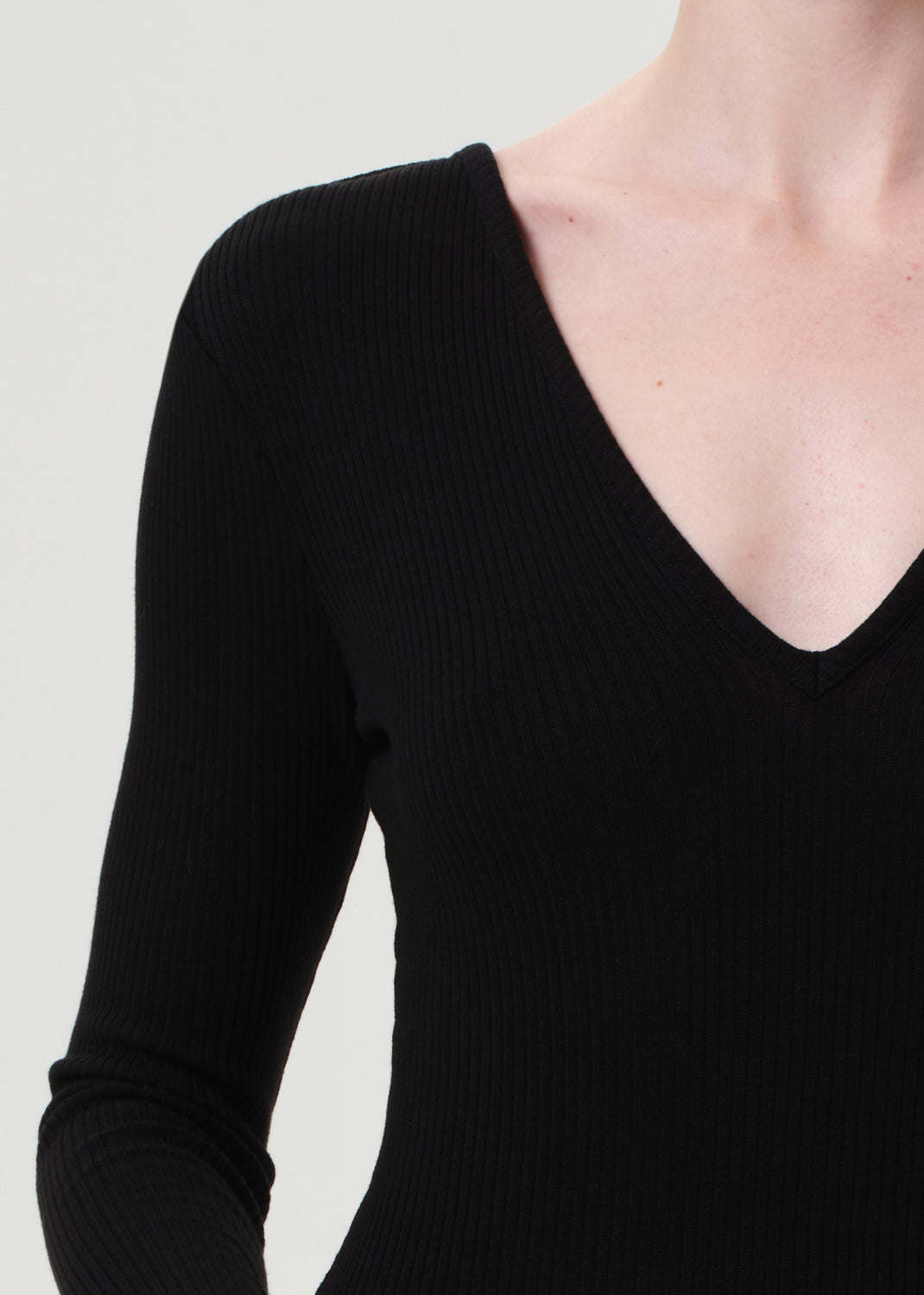 Black ribbed long-sleeve top worn by a person on a light gray background