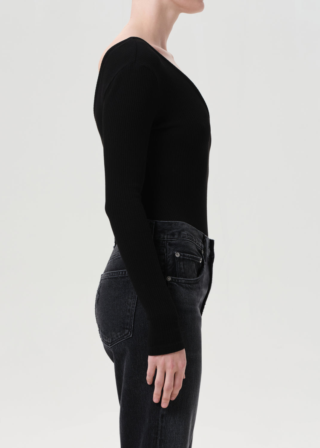 Person wearing a black long-sleeve top and dark jeans on a light gray background