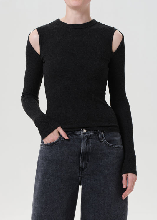 Person wearing a black long-sleeve top with cut-out shoulders and dark jeans on a light gray background