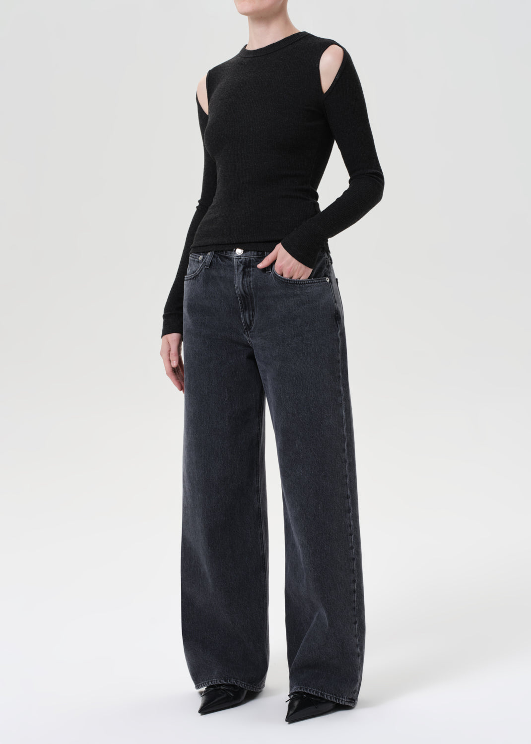 Person wearing a black long-sleeve top with cut-out shoulders and dark jeans on a white background