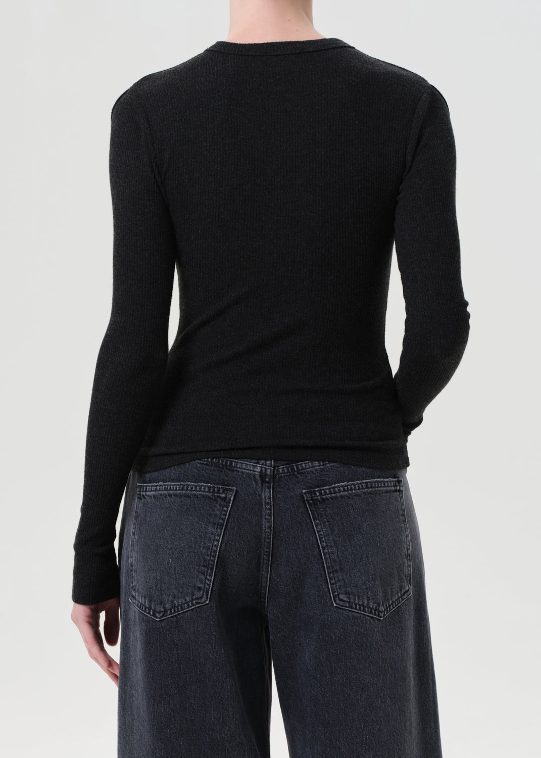 Person wearing a black long-sleeve shirt and dark jeans on a light gray background