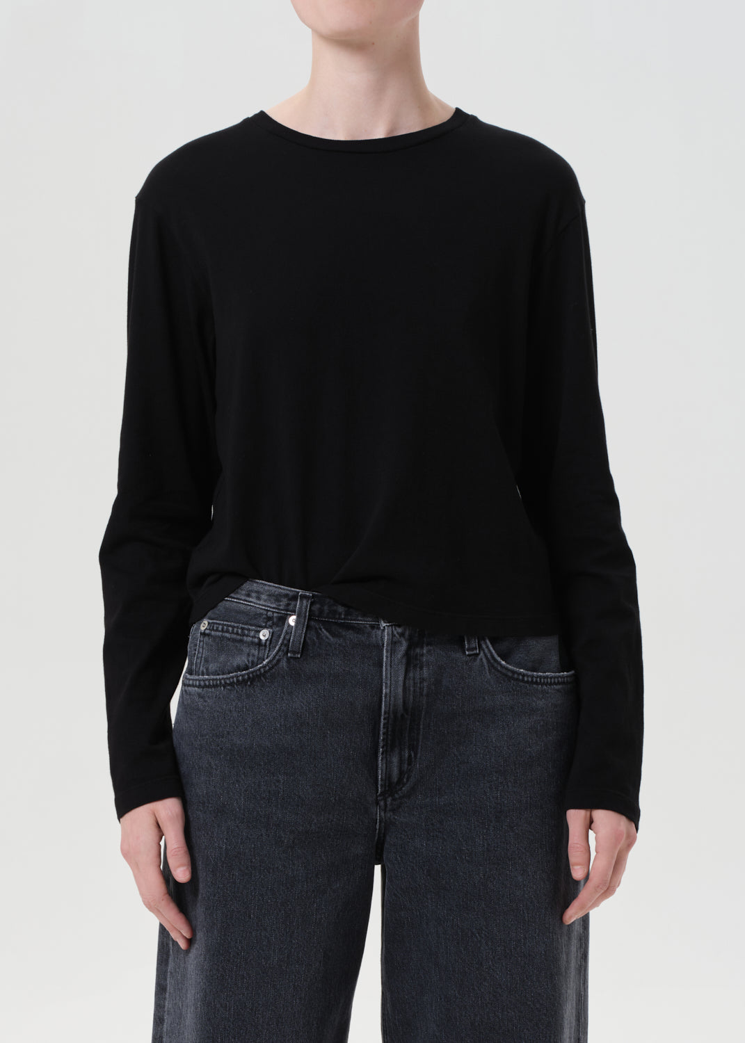 Person wearing a black long-sleeve shirt and dark jeans on a white background
