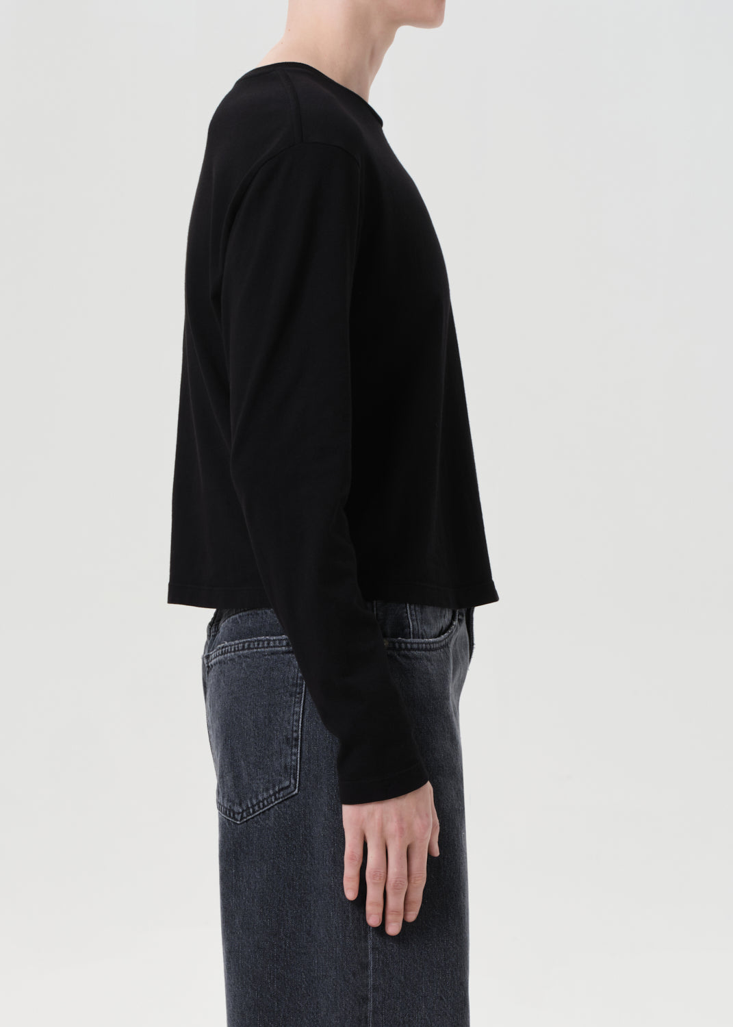 Person wearing a black long-sleeve shirt and blue jeans on a light gray background
