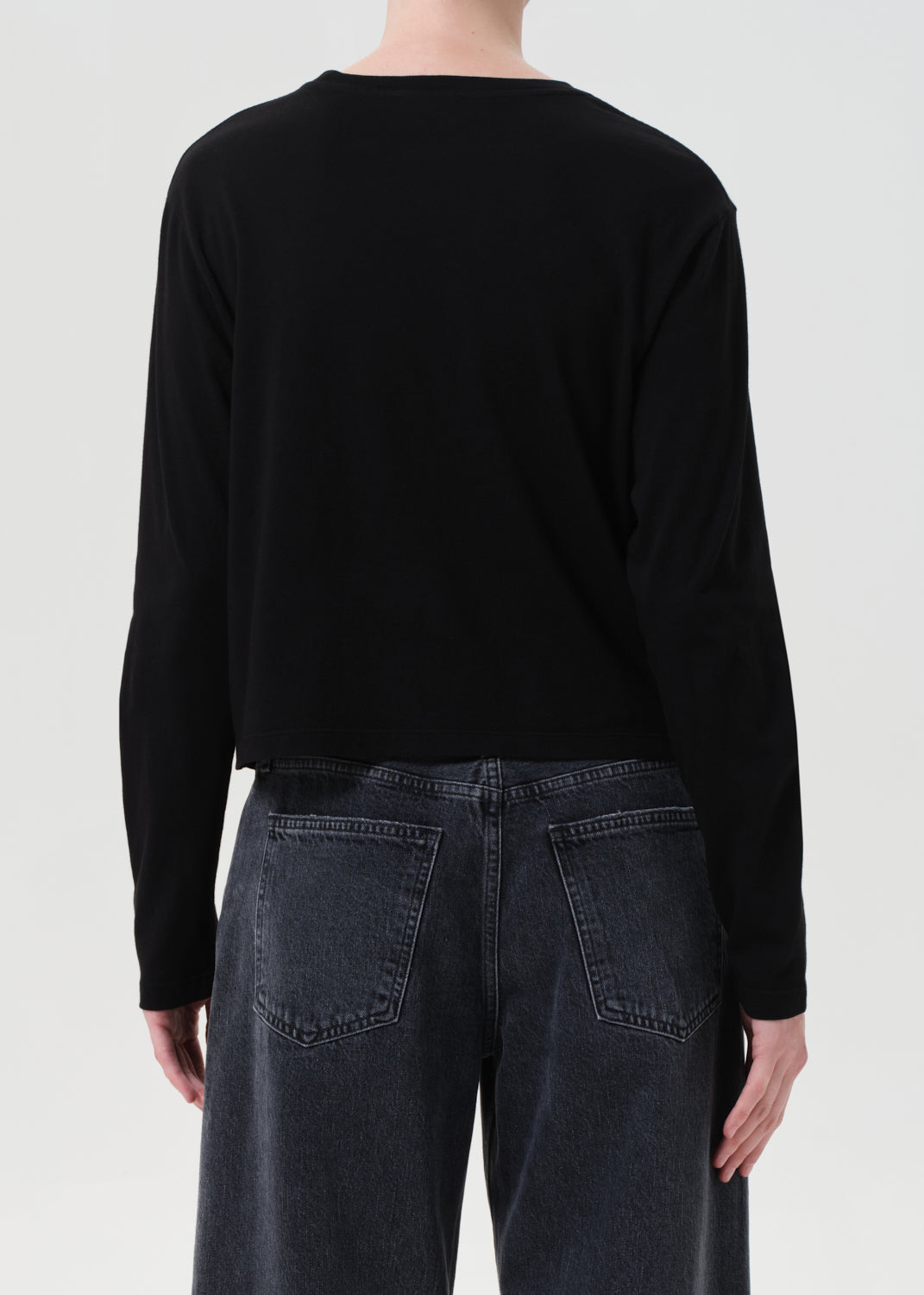 Person wearing a black long-sleeve shirt and dark jeans on a white background
