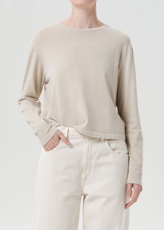 Person wearing a beige long-sleeve top and white pants on a light gray background